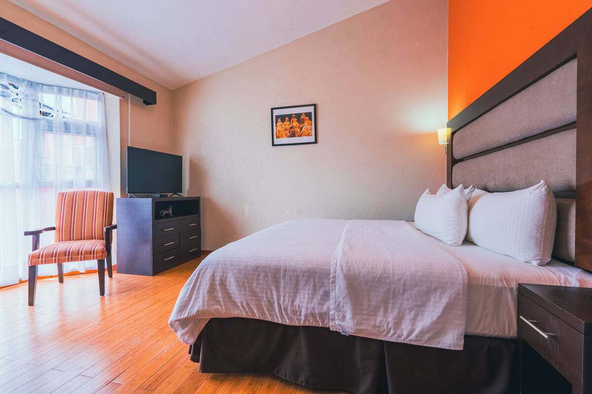 Una camera d'albergo con un letto, una sedia, una televisione e un quadro appeso al muro.