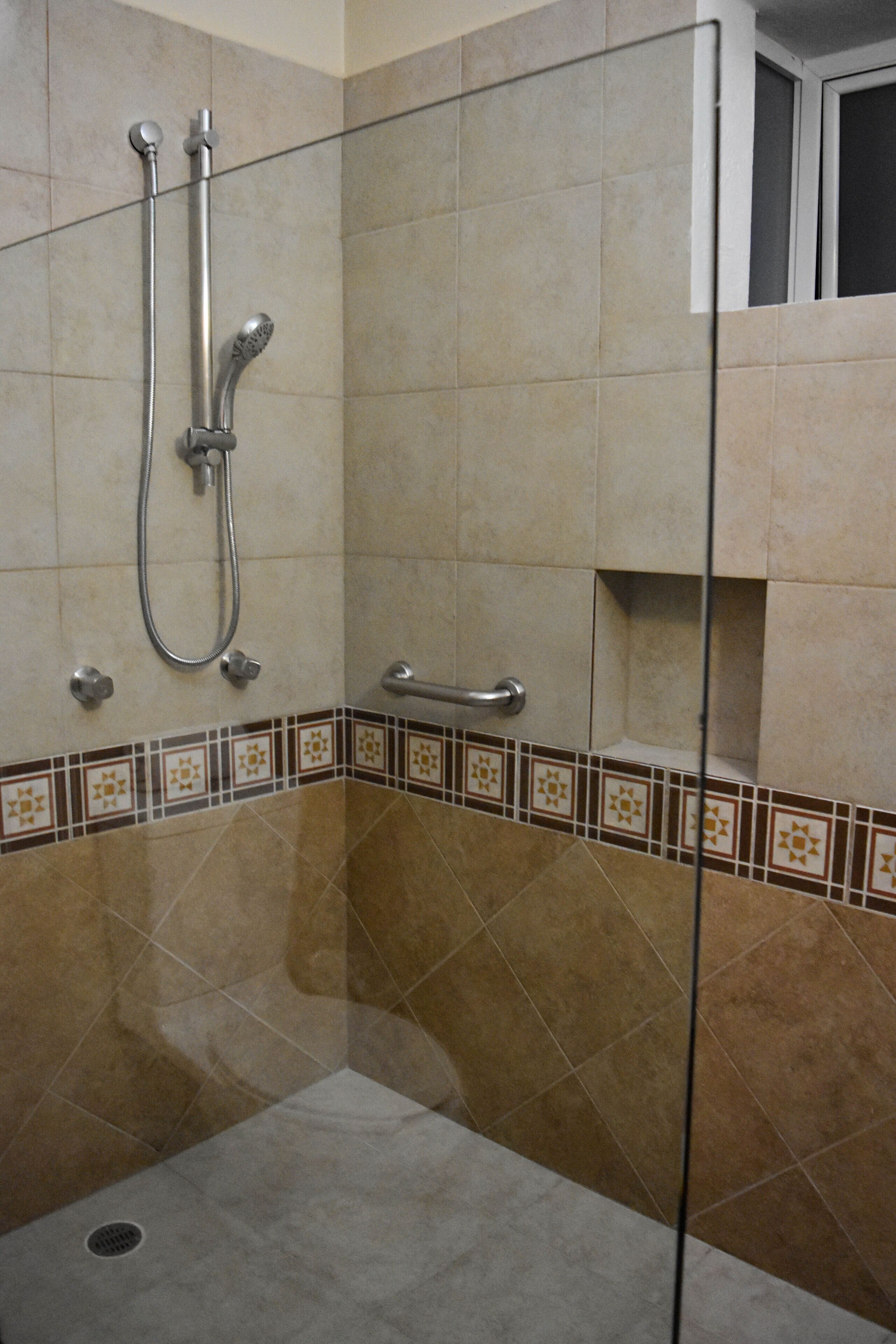 A shower area with a glass partition, tiled walls, and a handrail.