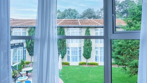 A room with large windows, a wooden floor, and a view of a house and garden.