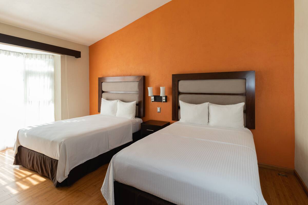 Camera d'albergo con due letti, un comodino e una lampada a parete.