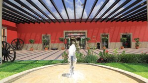 A courtyard with a fountain, potted plants, and a red building facade.