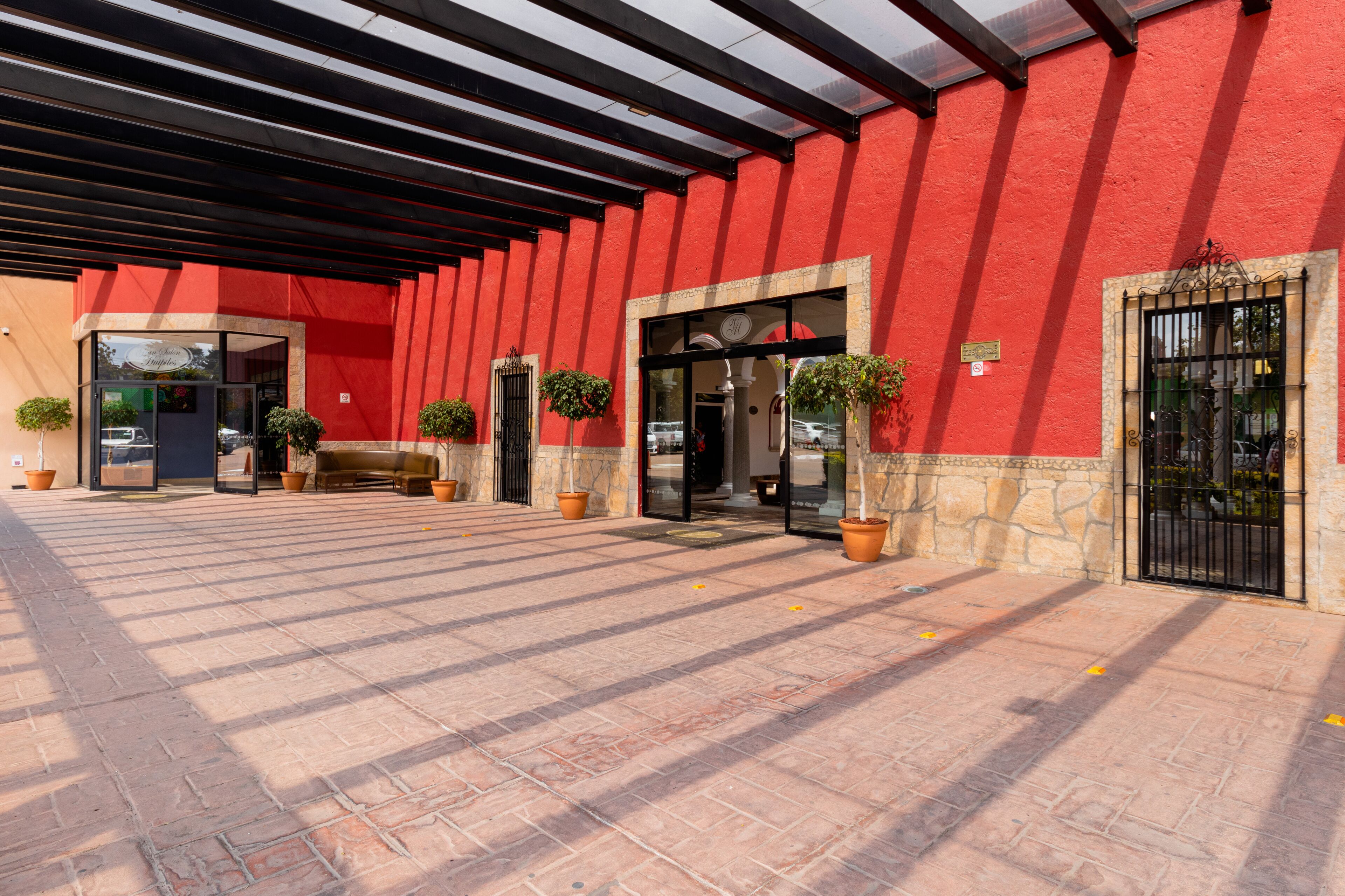 A red building with a covered entrance, potted plants, and a stone wall.