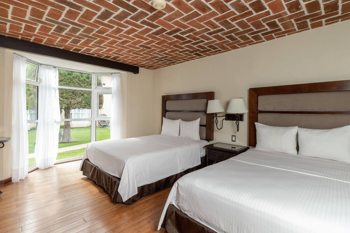 Una camera d'albergo con due letti, soffitto in mattoni, vista sull'esterno e pavimento in legno.