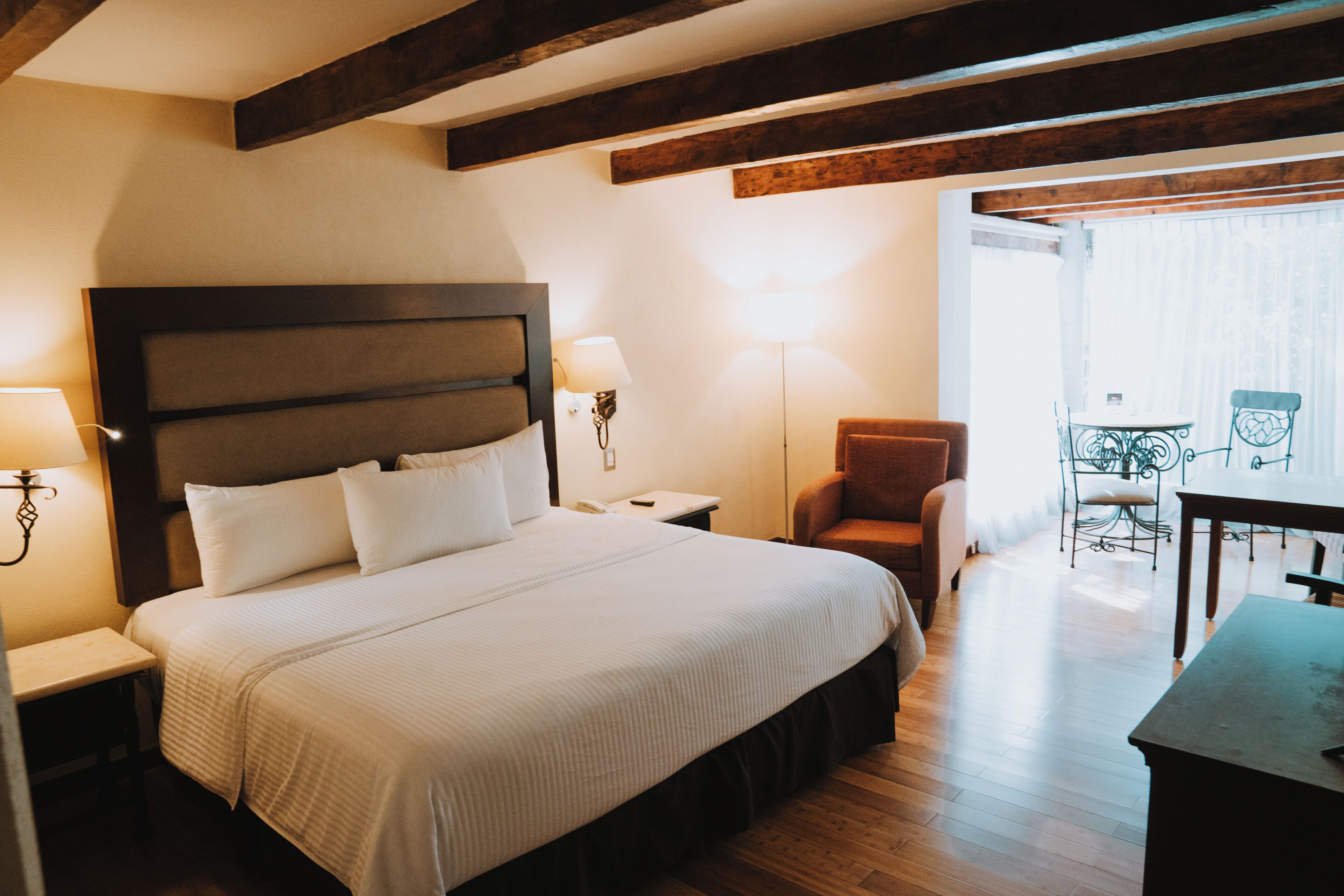 Habitación de hotel con una cama grande, una mesita de noche, una silla, una mesa y un balcón con vistas.