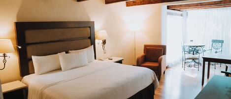 Habitación de hotel con una cama grande, una mesita de noche, una silla, una mesa y un balcón con vistas.