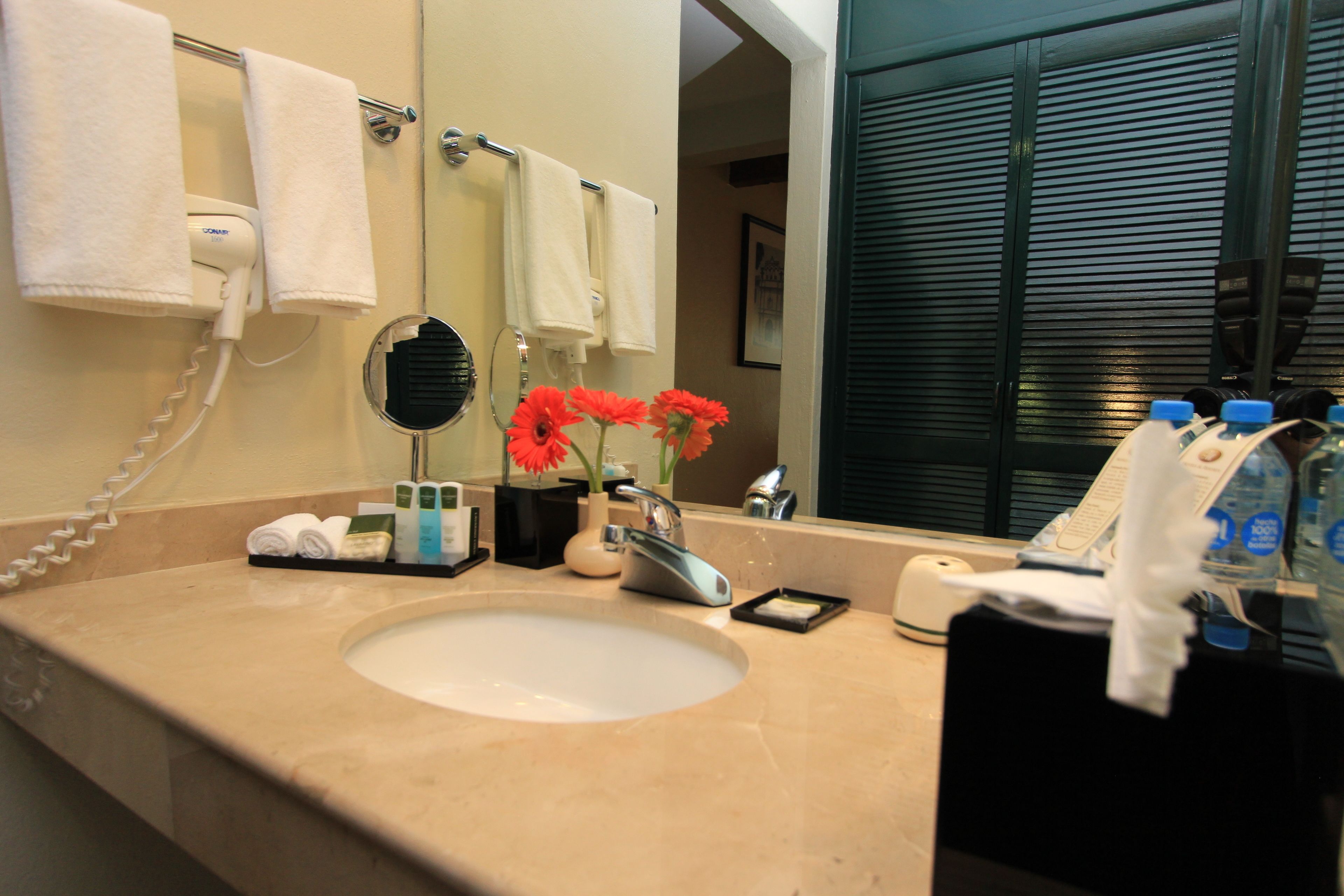 Un baño de hotel con lavamanos, espejo, toallero y artículos de aseo.
