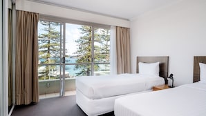 Habitación de hotel con dos camas, un ventanal con cortinas, una lámpara en el techo y vistas a árboles y agua.