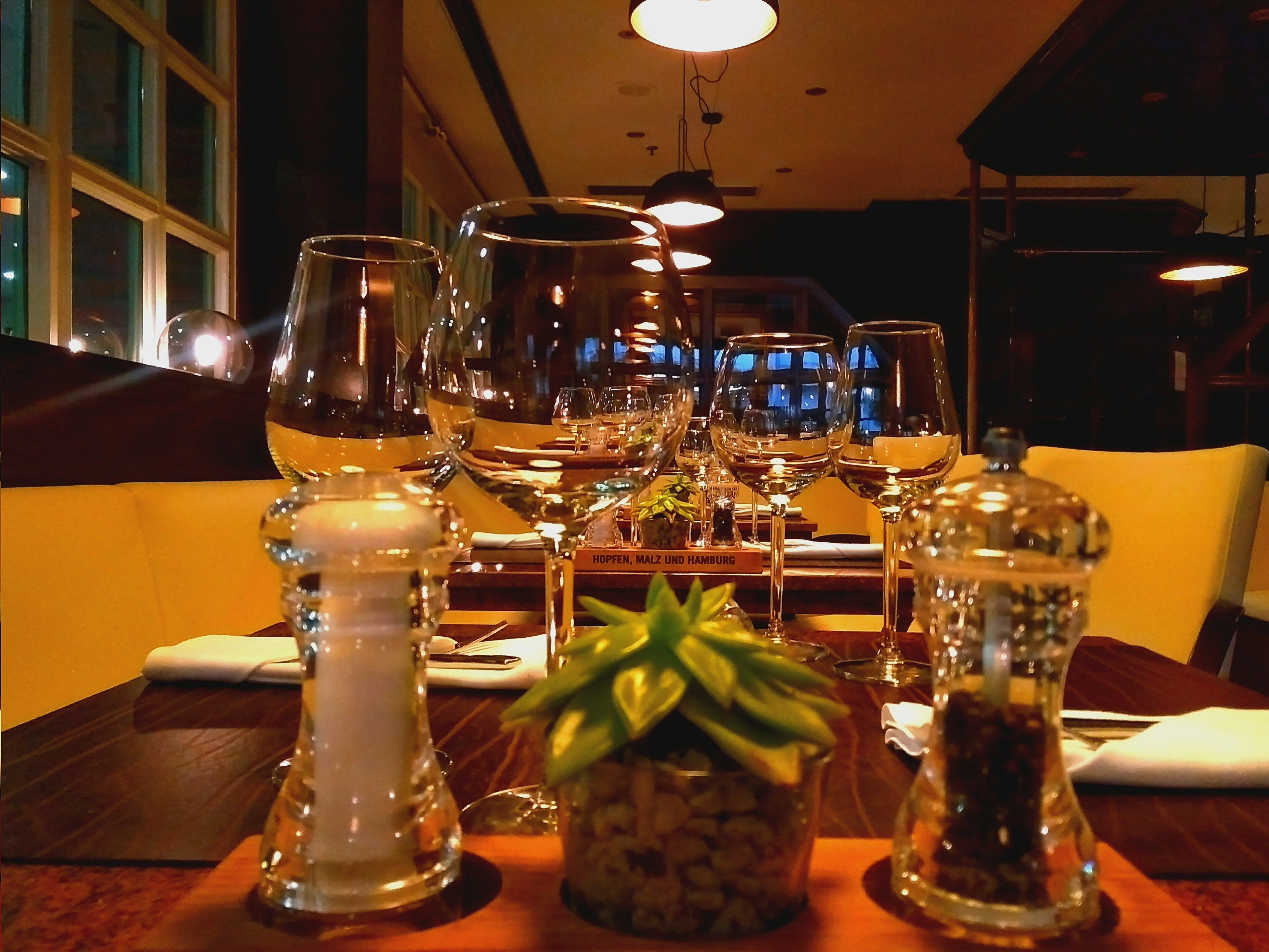 Une table à manger dressée avec plusieurs verres à vin, un salier et un poivrier, et une petite plante en pot.