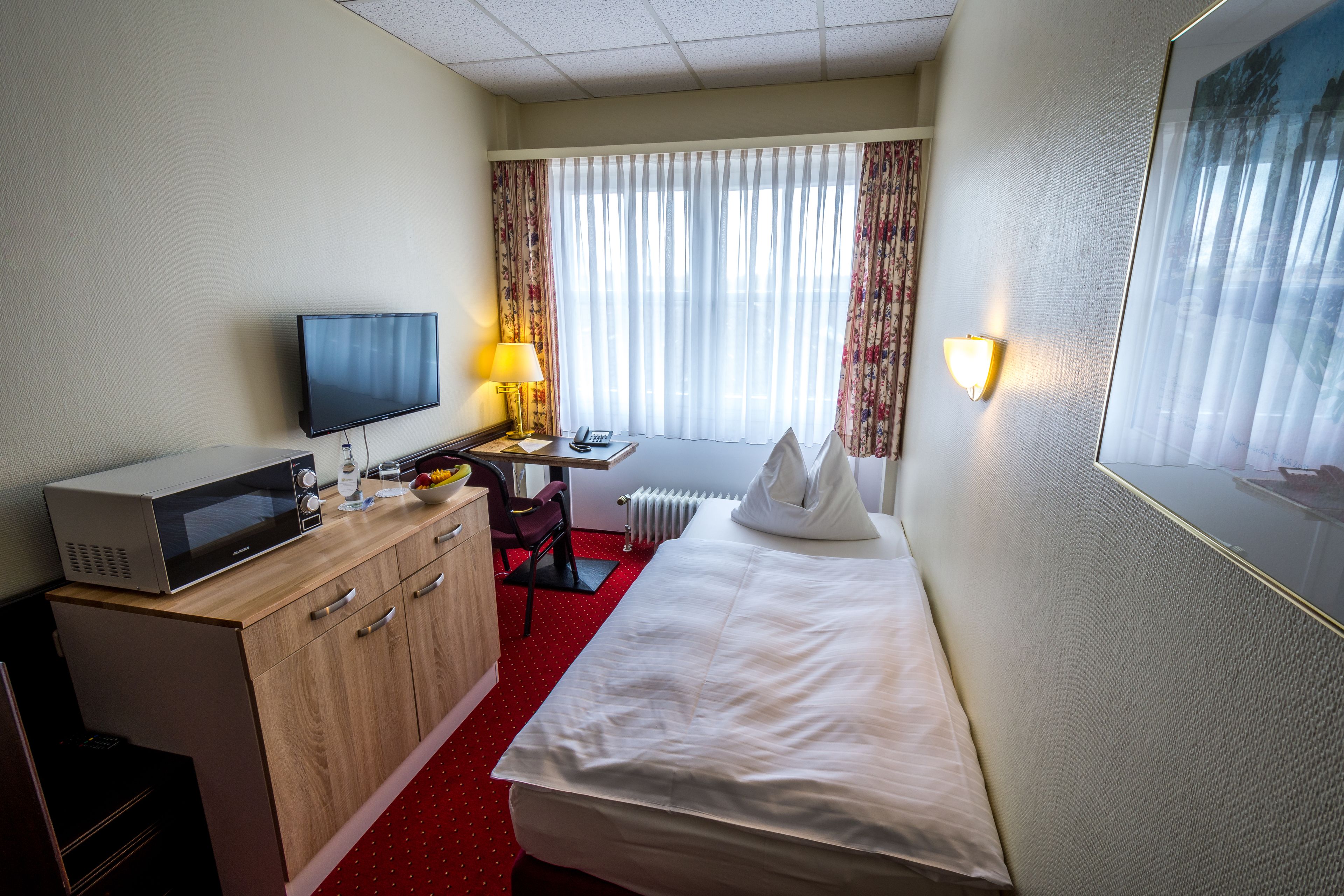 A hotel room with a bed, a desk with a computer, a microwave, and a TV.