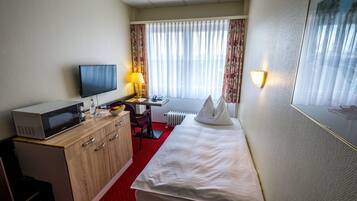 A hotel room with a bed, a desk with a computer, a microwave, and a TV.