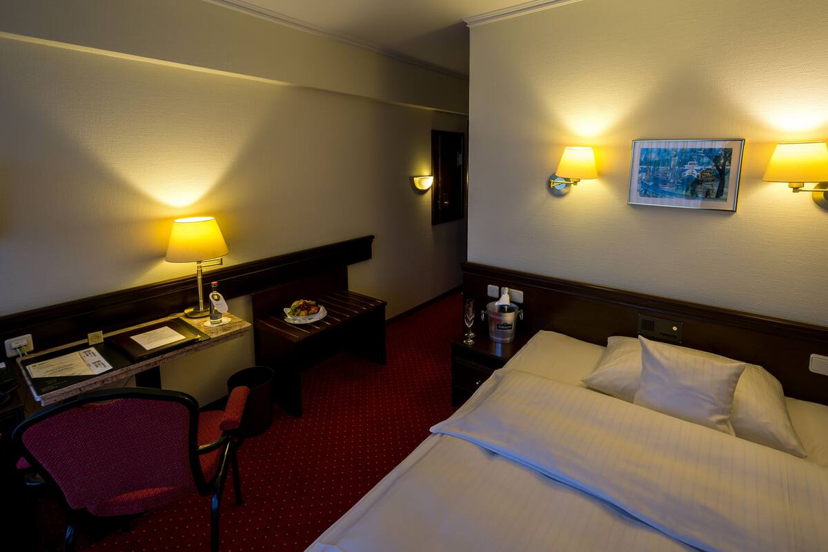 Ein Hotelzimmer mit einem Bett, einem Schreibtisch mit Stuhl, einem kleinen Tisch mit Teller und zwei Wandlampen.