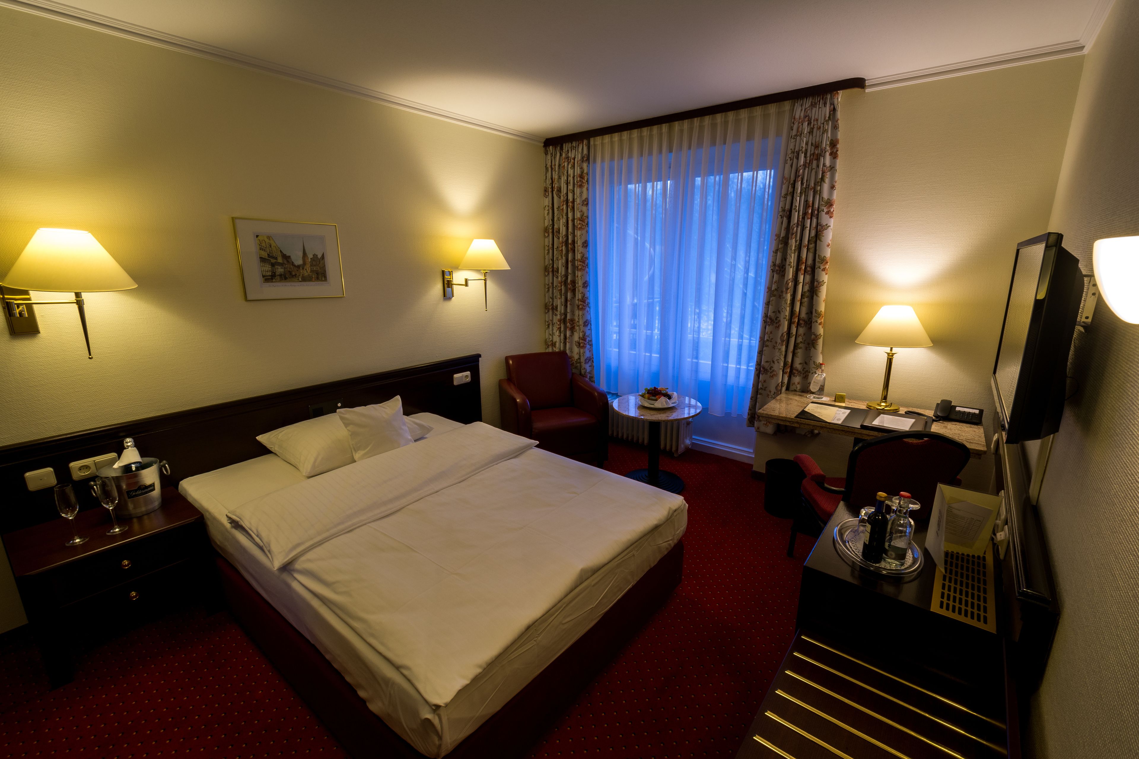 Habitación de hotel con una cama grande, dos lámparas de noche, un escritorio con silla, una mesita y un televisor.
