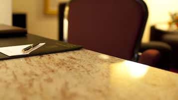 A close-up of a marble table with a pen and a piece of paper, a red chair, and a lamp in the background.