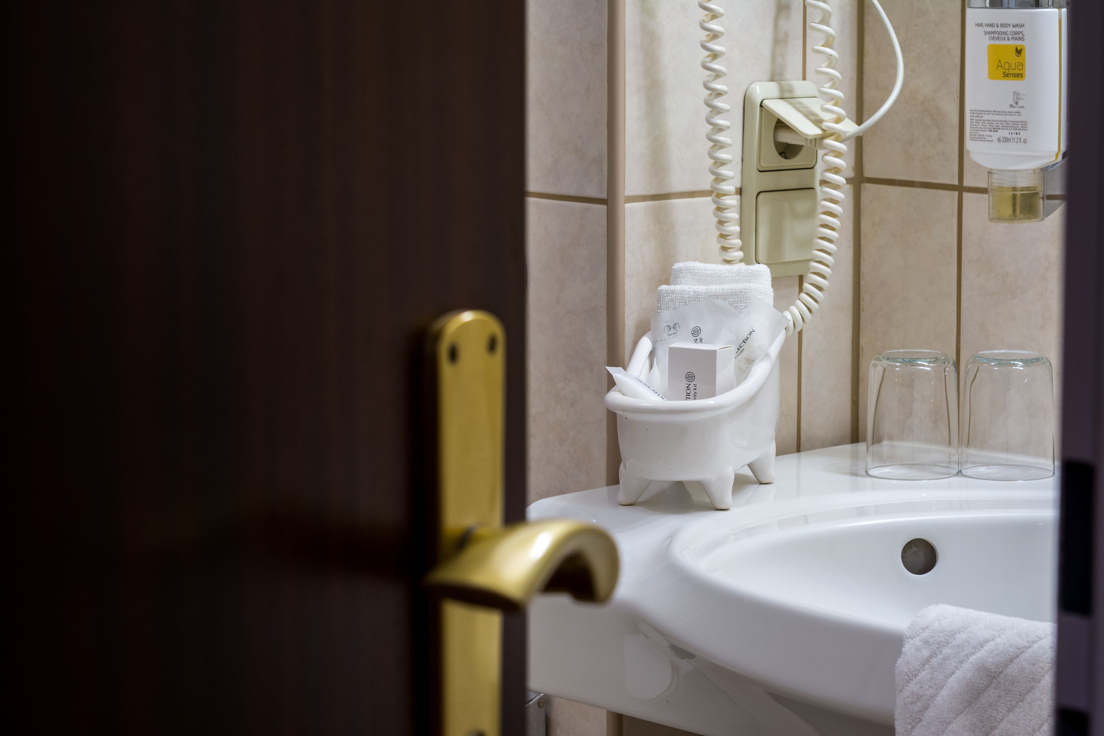 Un baño con un lavabo blanco, una toalla, un dispensador de jabón de vidrio y un teléfono.