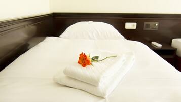 A neatly made bed with a folded white towel and a single rose.