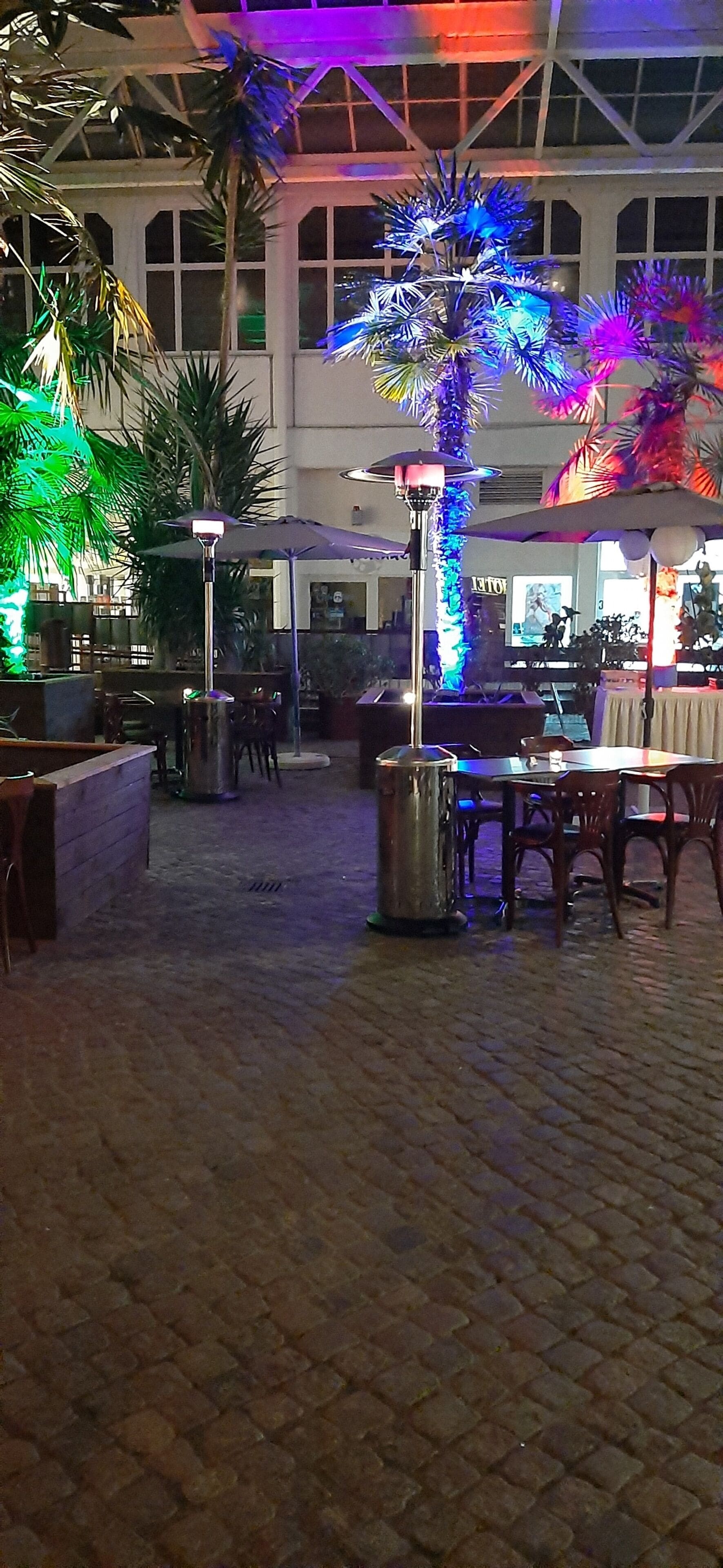 An indoor courtyard with brick flooring, tables, chairs, and decorative lighting.