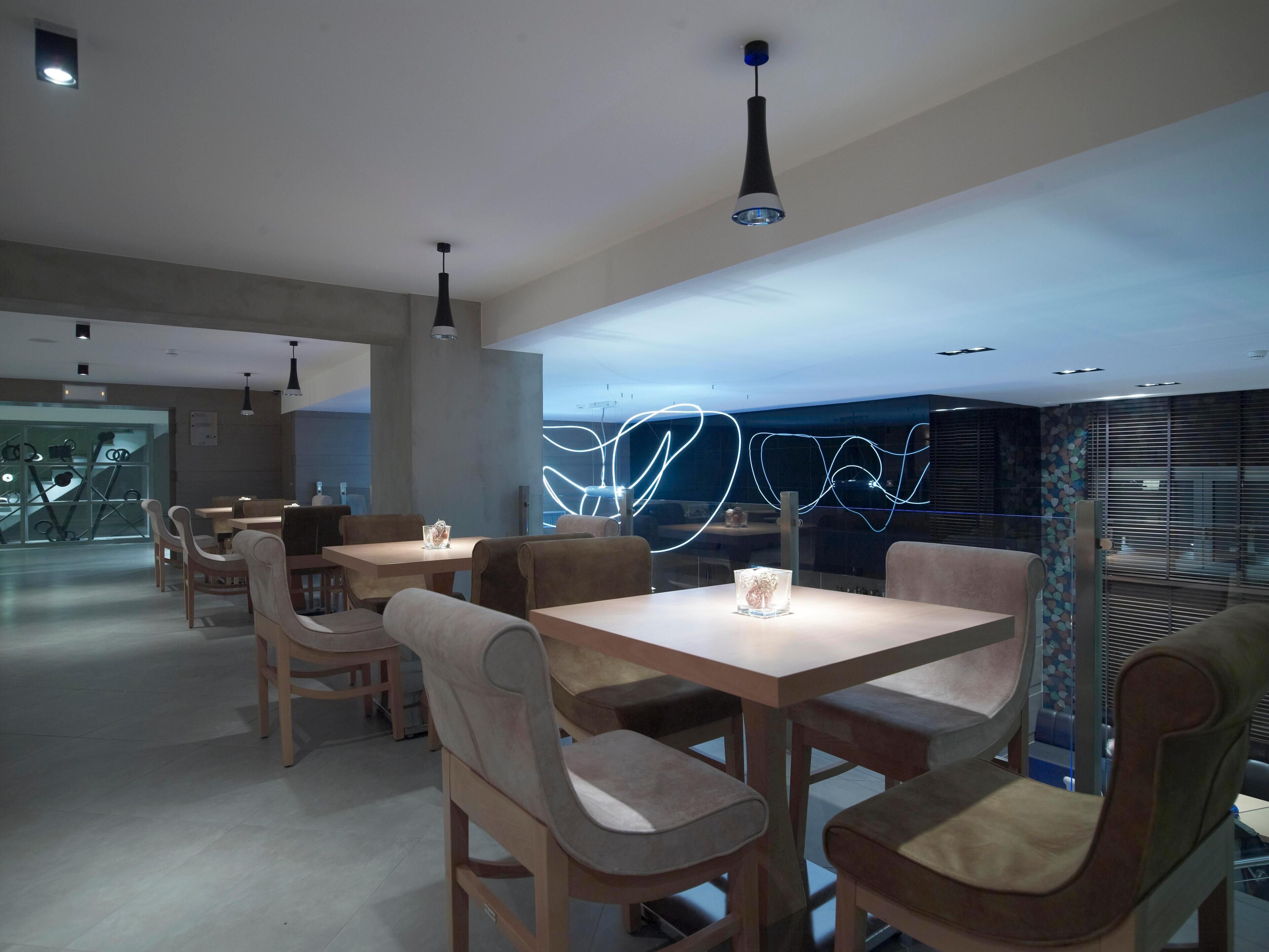 A modern dining area with tables and chairs, pendant lighting, and a wall with abstract light patterns.
