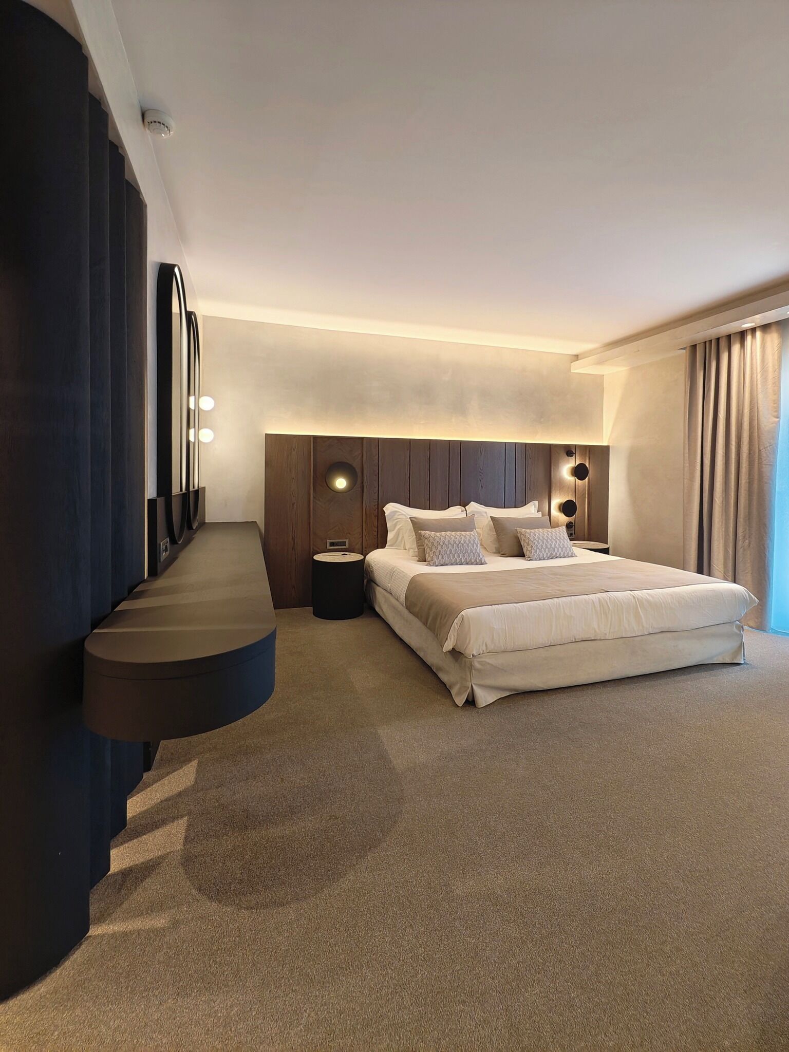 A modern hotel room with a large bed, a built-in desk, and a large mirror.