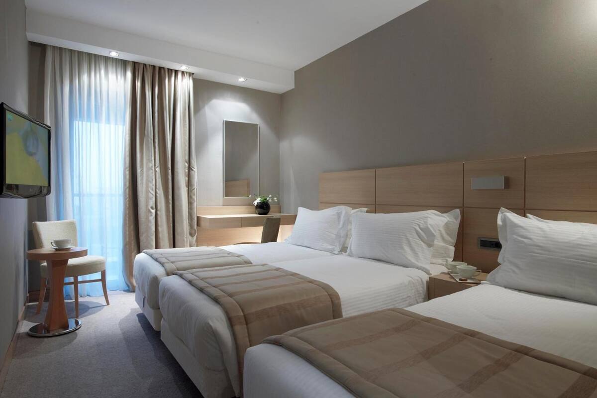 Habitación de hotel con dos camas, un escritorio, una silla, un televisor y un ventanal con cortinas.