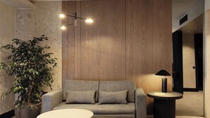 A modern living room with a grey sofa, two round coffee tables, a potted plant, and a wooden wall panel. - Anatolia Hotel (Komotini)