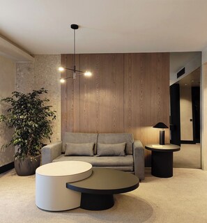 Una sala de estar moderna con un sofá gris, dos mesas redondas de centro, una planta en maceta y un panel de pared de madera.