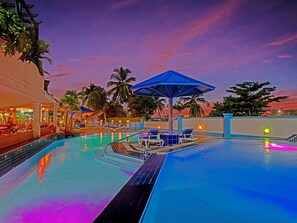 A pool area with lounge chairs and umbrellas, surrounded by palm trees and a sunset sky. - The Atrium Beach Resort and Spa, an Ascend Collection Resort (Simpson Bay)