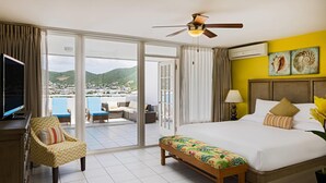 Habitación de hotel con una cama grande, un banco, un televisor y vistas de la ciudad a través de puertas correderas.