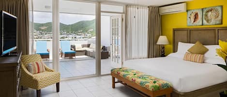 Habitación de hotel con una cama grande, un banco, un televisor y vistas de la ciudad a través de puertas correderas.