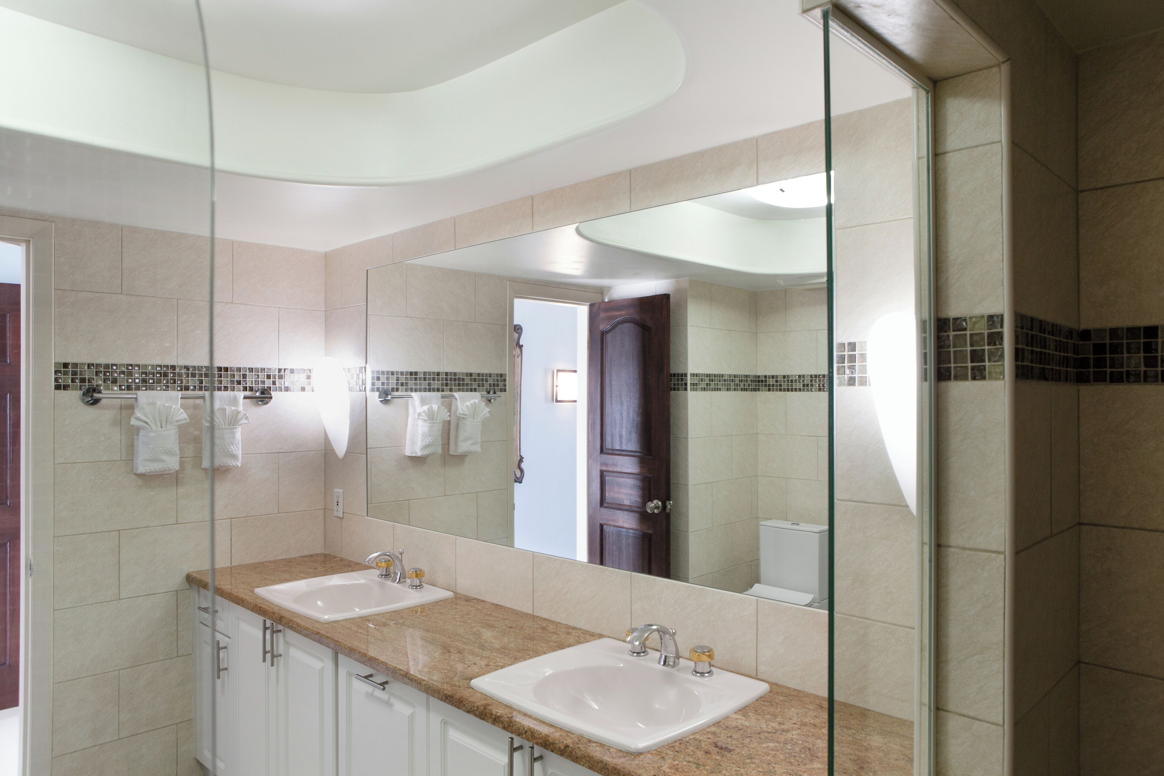 A modern bathroom with two sinks, a large mirror, and a glass shower enclosure.