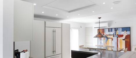 A modern kitchen with white cabinetry, a stainless steel refrigerator, and a black sink.