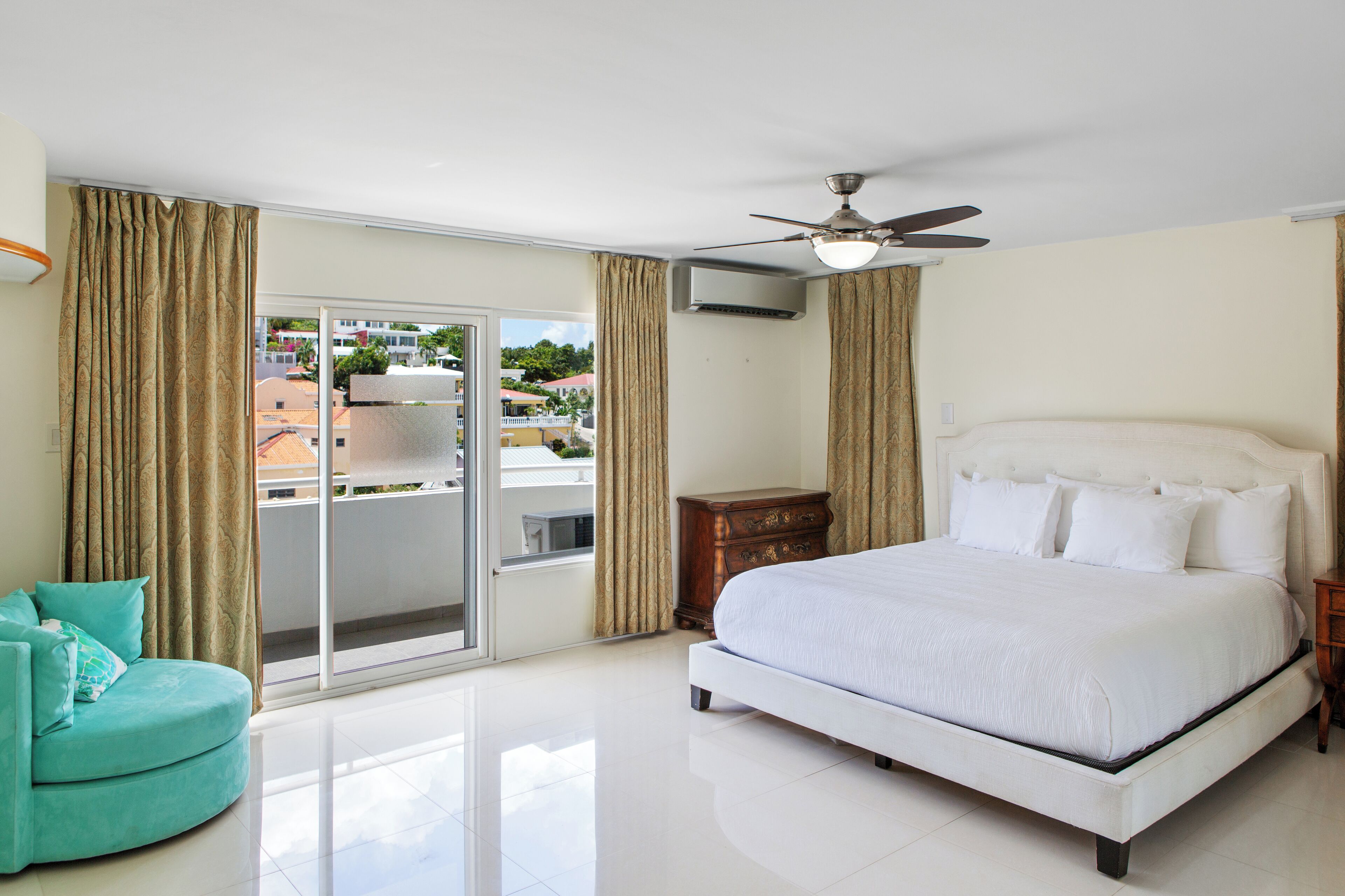 A bedroom with a large bed, a ceiling fan, and a view of a cityscape through a sliding glass door.