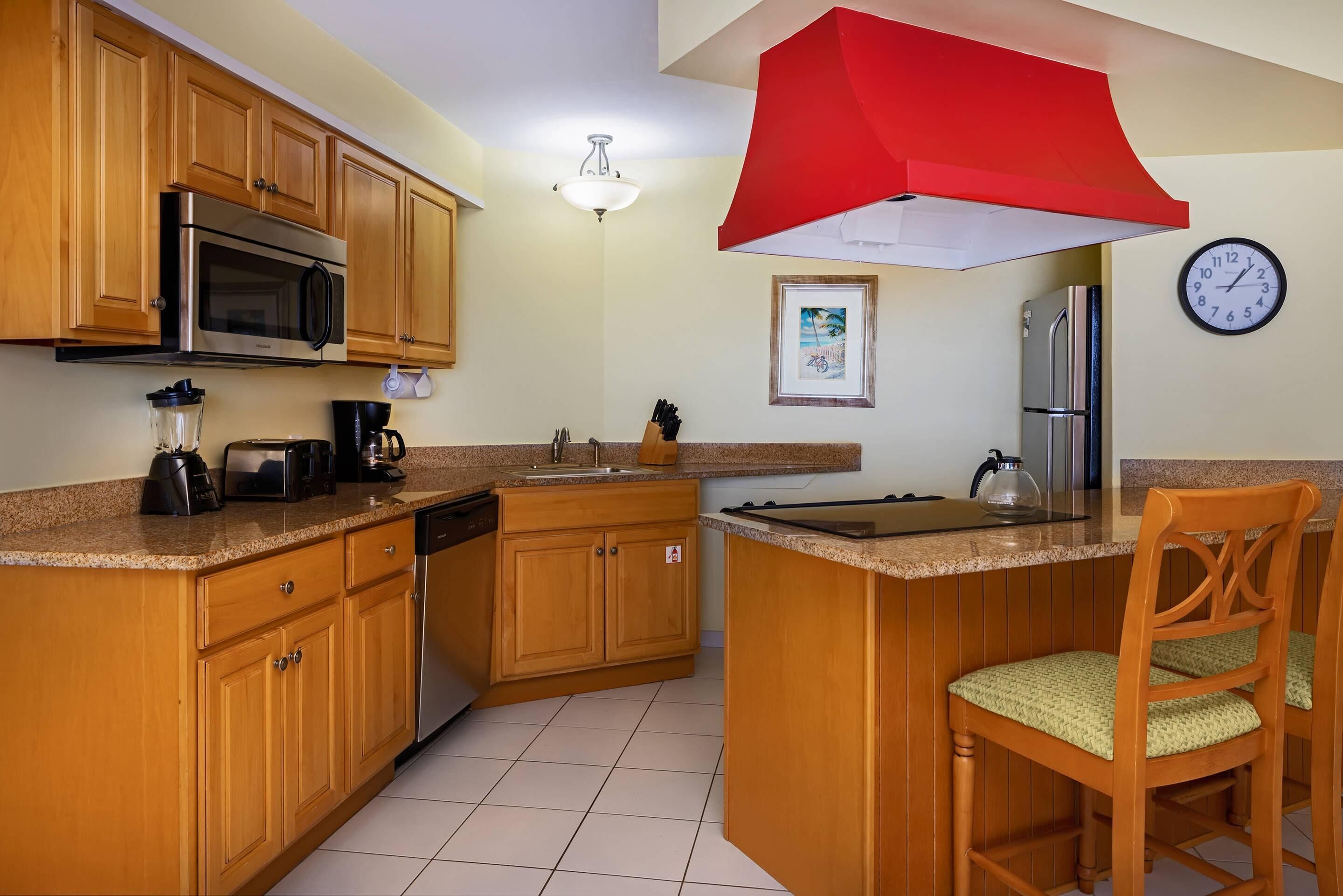 A kitchen with wooden cabinets, a stainless steel microwave, a coffee maker, and a red overhead light.