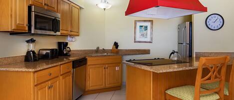 A kitchen with wooden cabinets, a stainless steel microwave, a coffee maker, and a red overhead light.