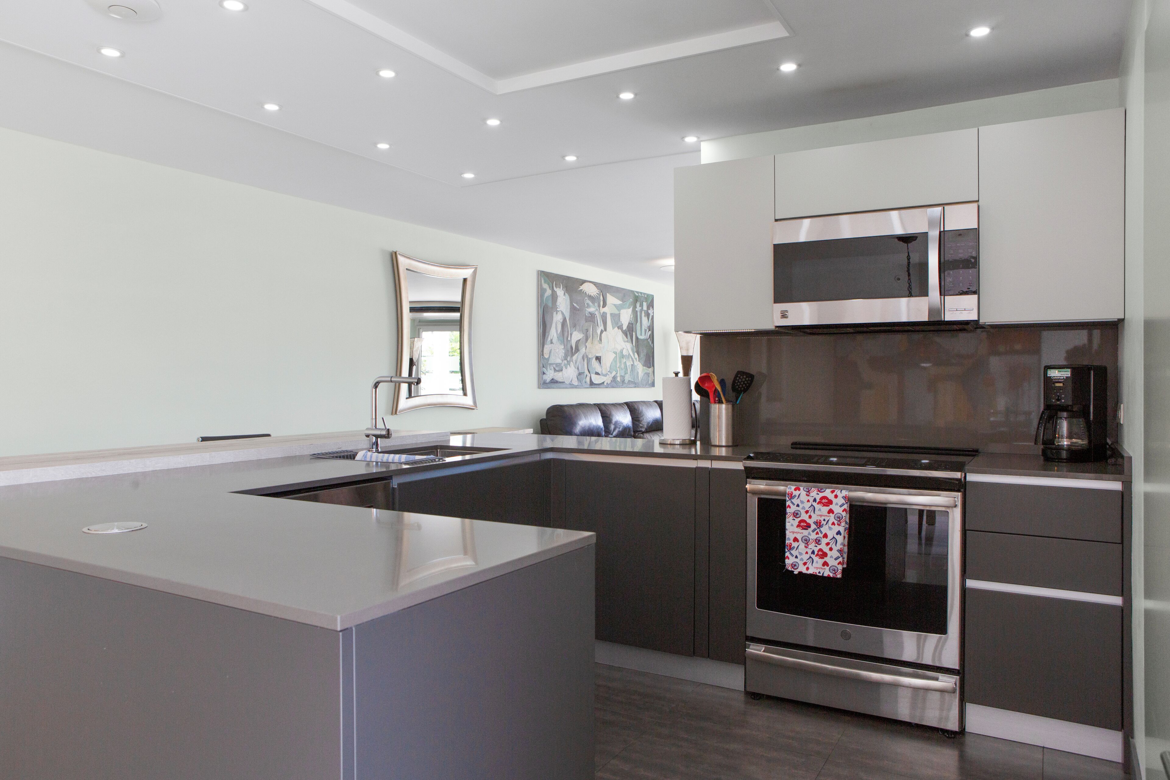 Una cocina moderna con una isla central, electrodomésticos de acero inoxidable y un espejo grande sobre el lavamanos.