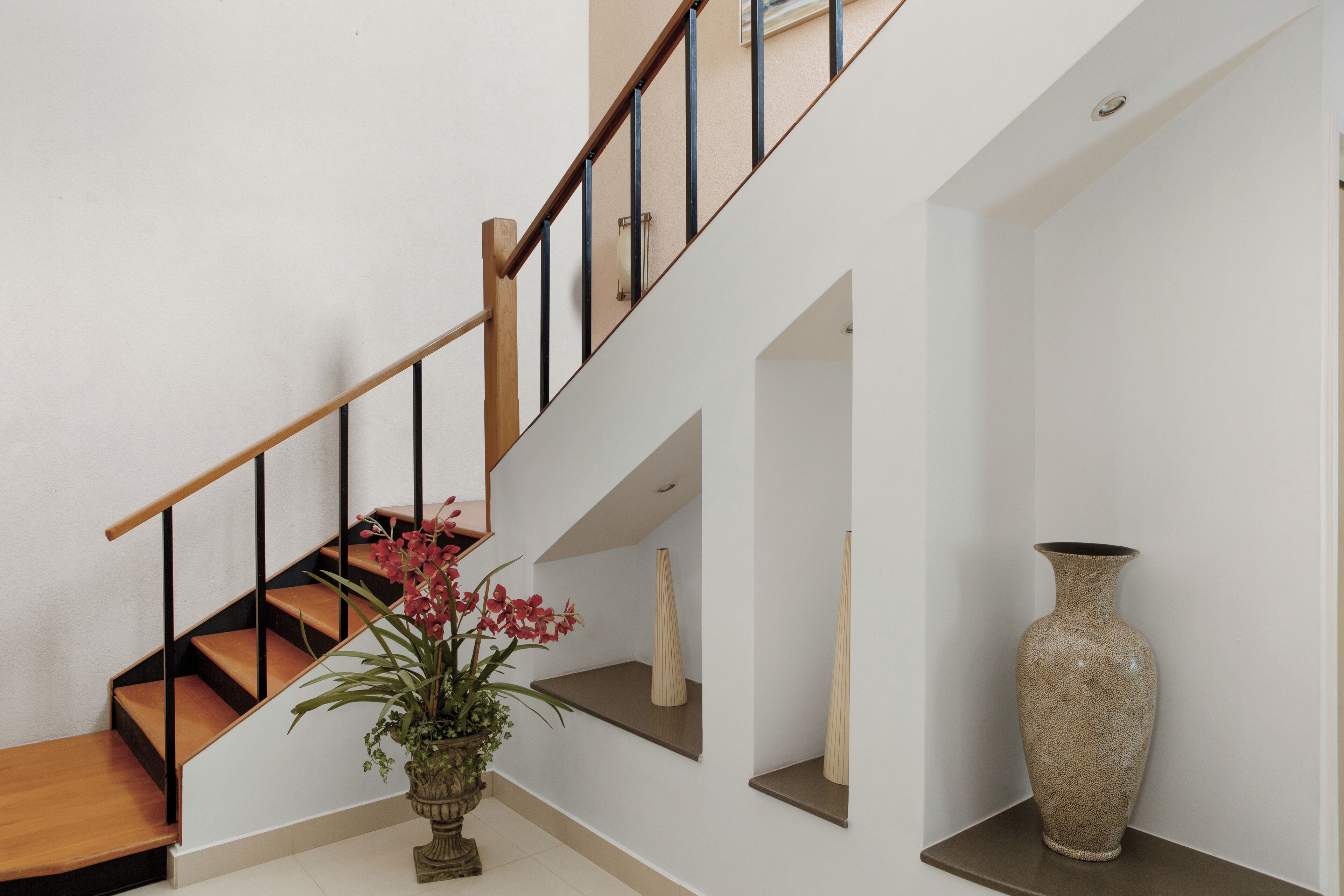 A staircase with wooden steps and black railings, a potted plant with red flowers, and a tall vase on a shelf.