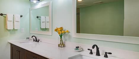 A bathroom with two sinks, a mirror, and a vase with yellow flowers.