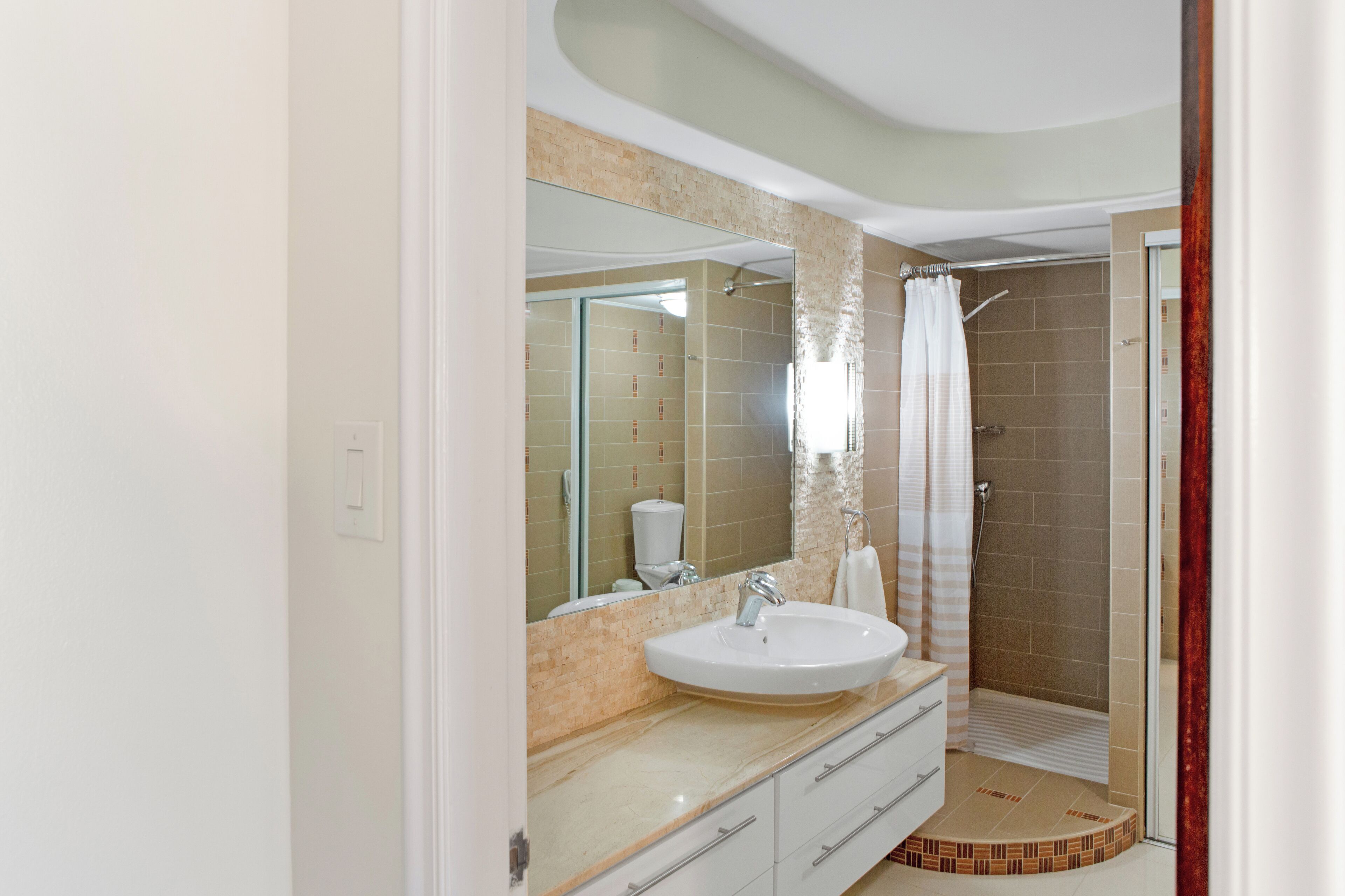 Une salle de bain moderne dotée d’un grand lavabo, d’un miroir et d’un espace douche.