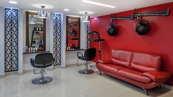 A modern salon with two black salon chairs, a red leather sofa, and a wall-mounted hairdryer.