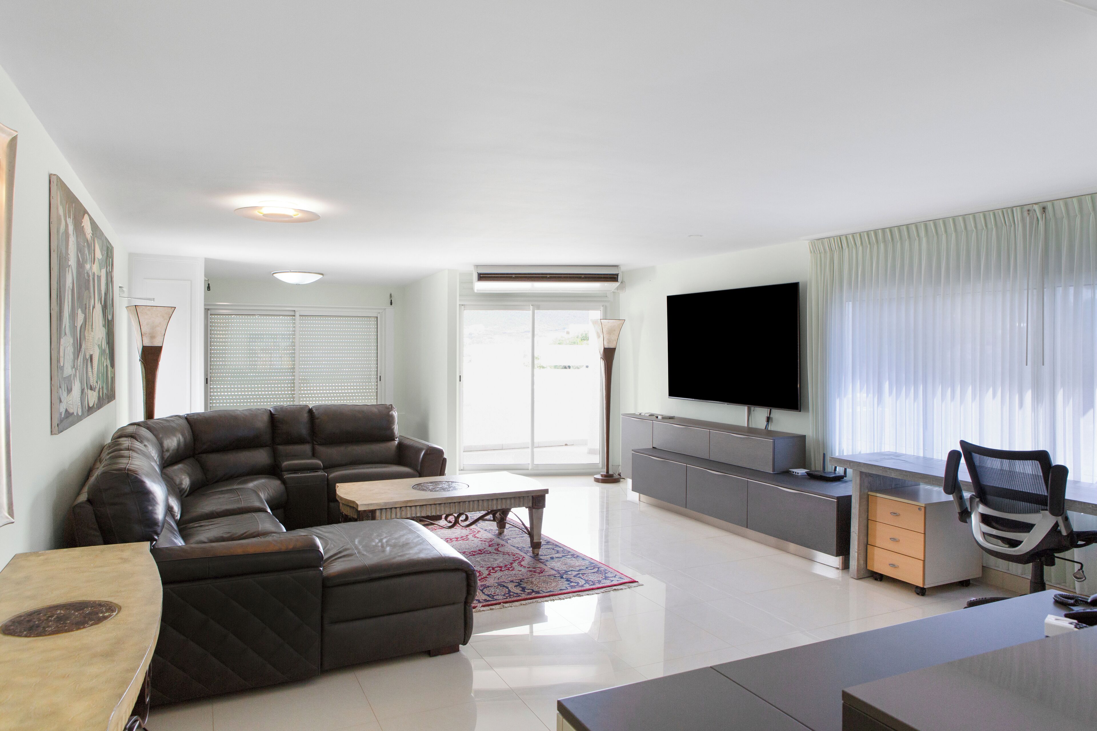 A modern living room with a leather sofa, a wooden coffee table, and a flat-screen TV mounted on the wall.