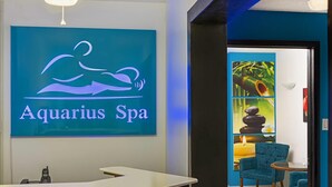 Interior de un spa con un mostrador de recepción, una silla azul y una pared con un letrero que dice "Aquarius Spa".