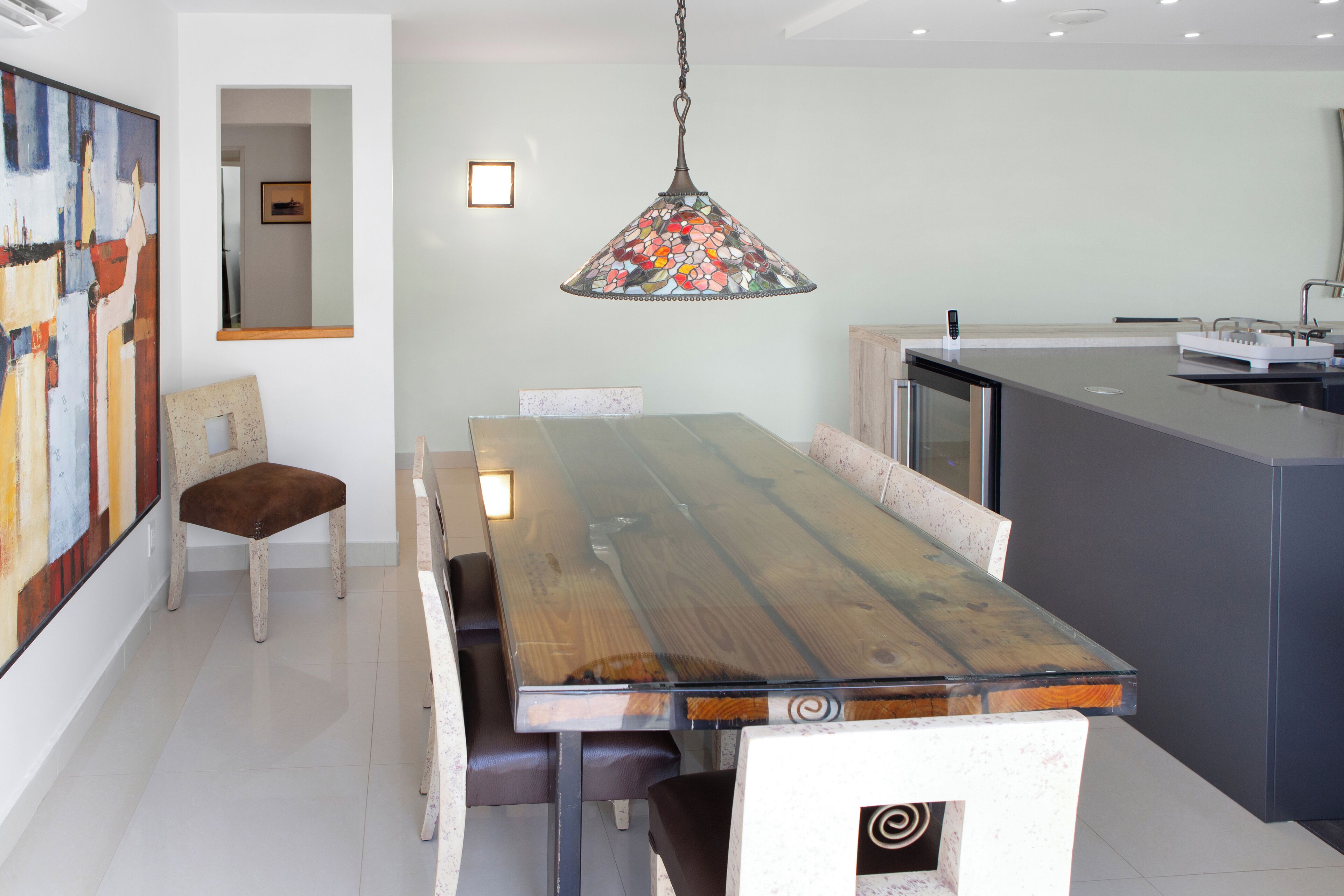 Un comedor moderno con una mesa y sillas de madera, una lámpara colgante con flores y una cocina con encimera y fregadero.