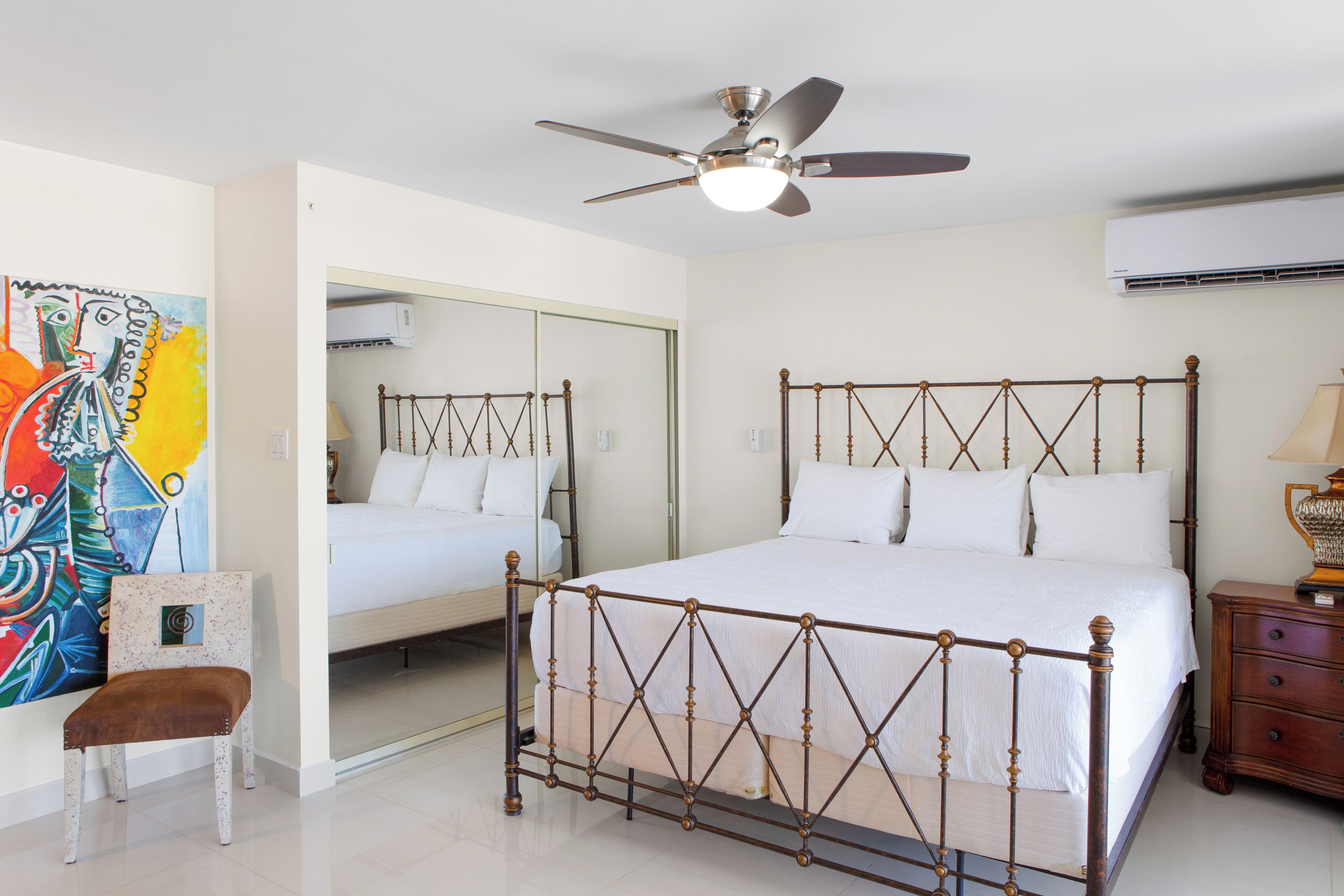 Un dormitorio con una cama grande, un ventilador de techo, una mesita de noche y una silla.