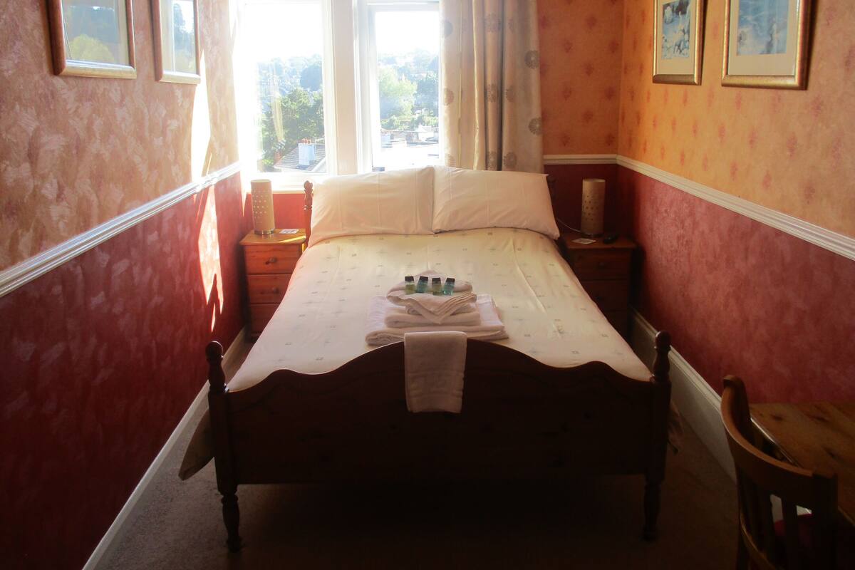 Un dormitorio con una cama, una mesita de noche, una silla de madera y una ventana con cortinas.