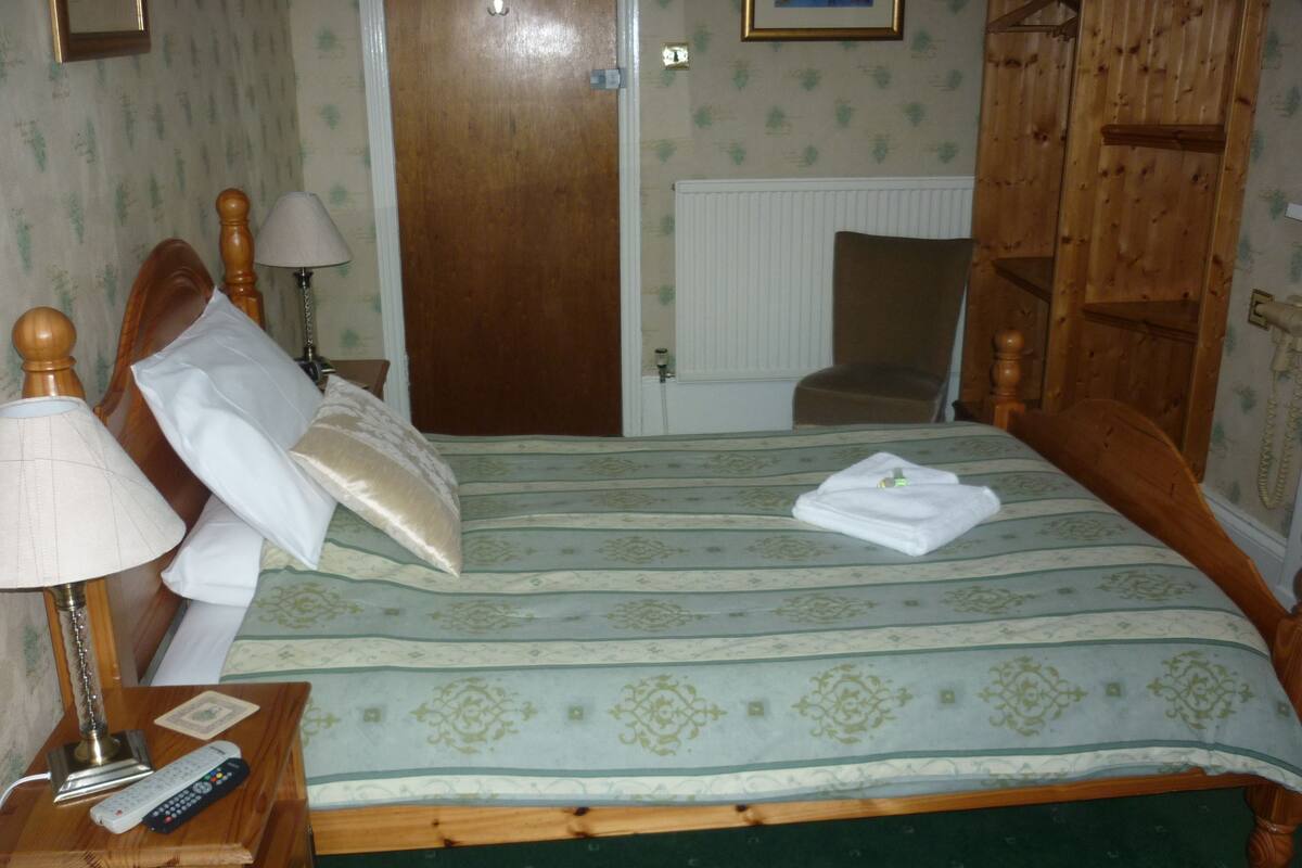 Una cama bien hecha con una colcha a rayas, una lámpara de noche, un control remoto y una toalla doblada sobre la cama.
