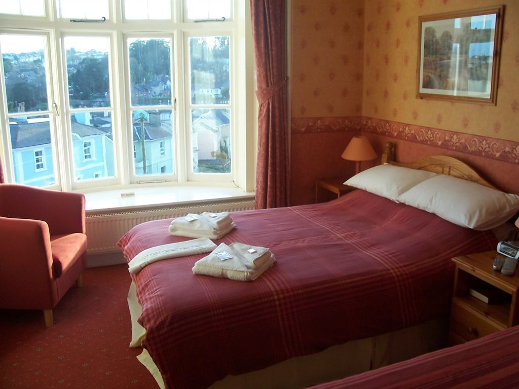 Habitación de hotel con una cama grande, una silla, una mesita de noche y una ventana con vistas a edificios.