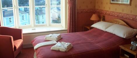 Habitación de hotel con una cama grande, una silla, una mesita de noche y una ventana con vistas a edificios.