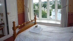 Ein Schlafzimmer mit einem hölzernen Bett, einem Fenster mit Vorhängen und Blick auf Gebäude.