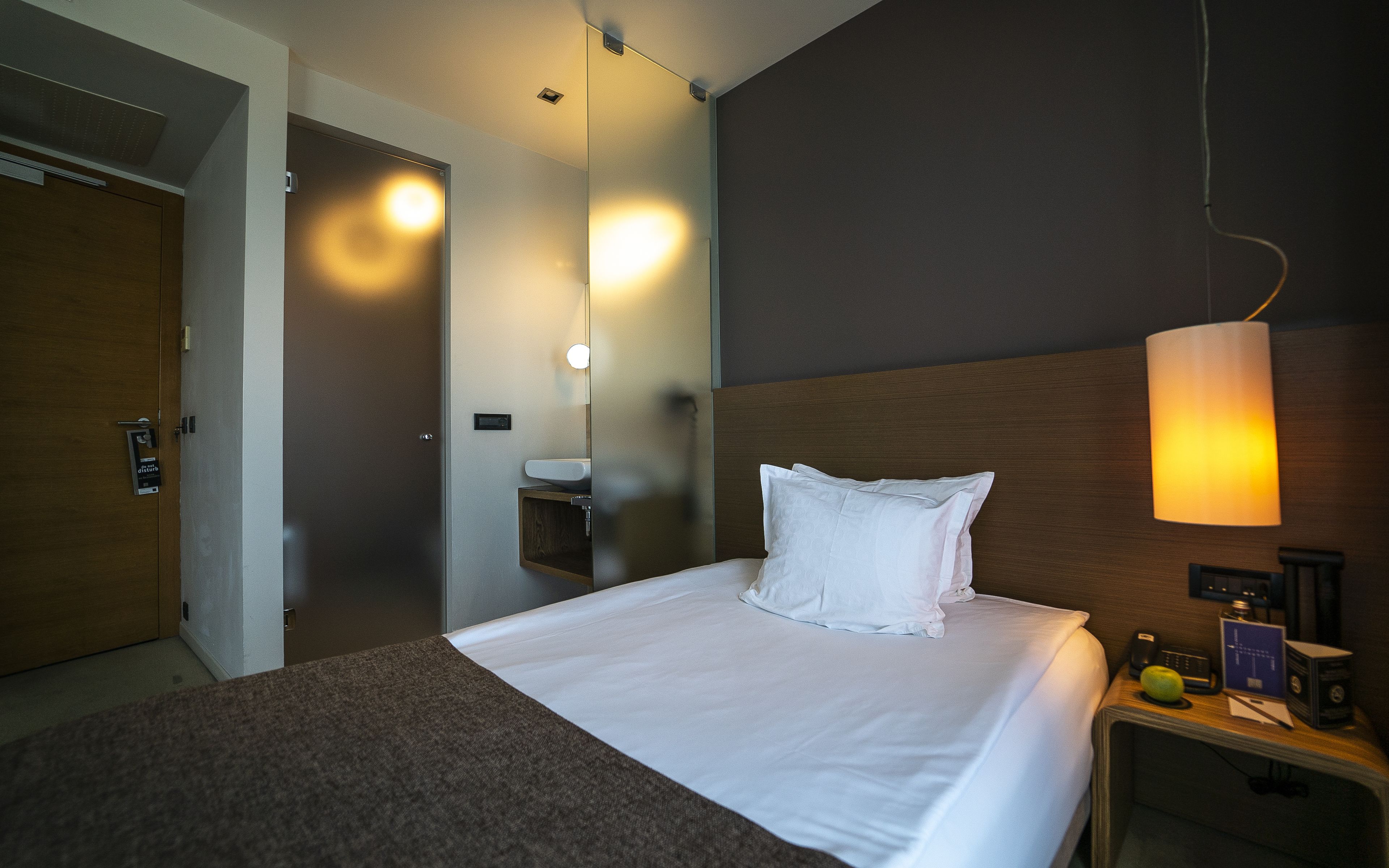 A hotel room with a bed, bedside table, lamp, and a mirror.