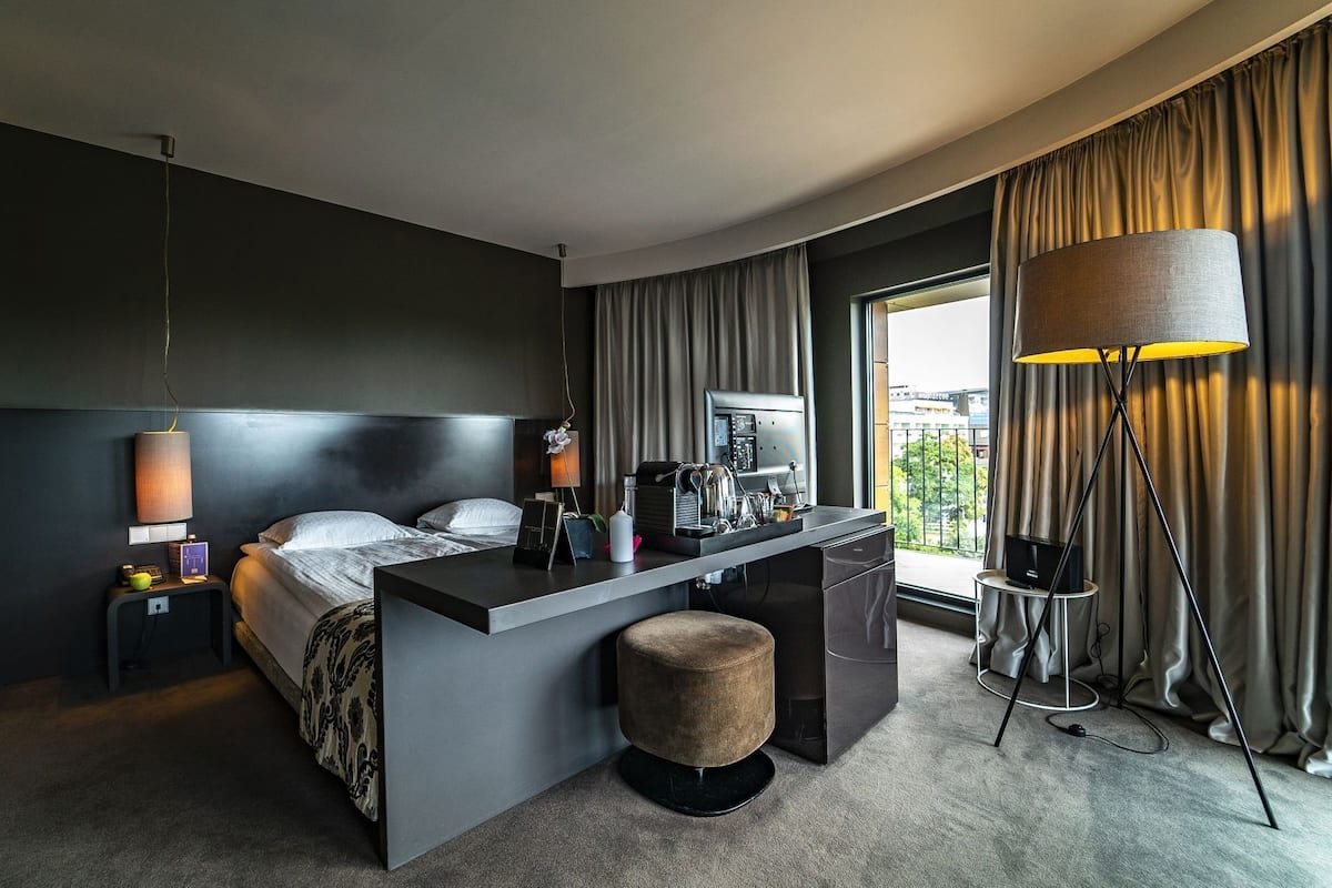 A modern hotel room with a bed, desk, and a large window with curtains.