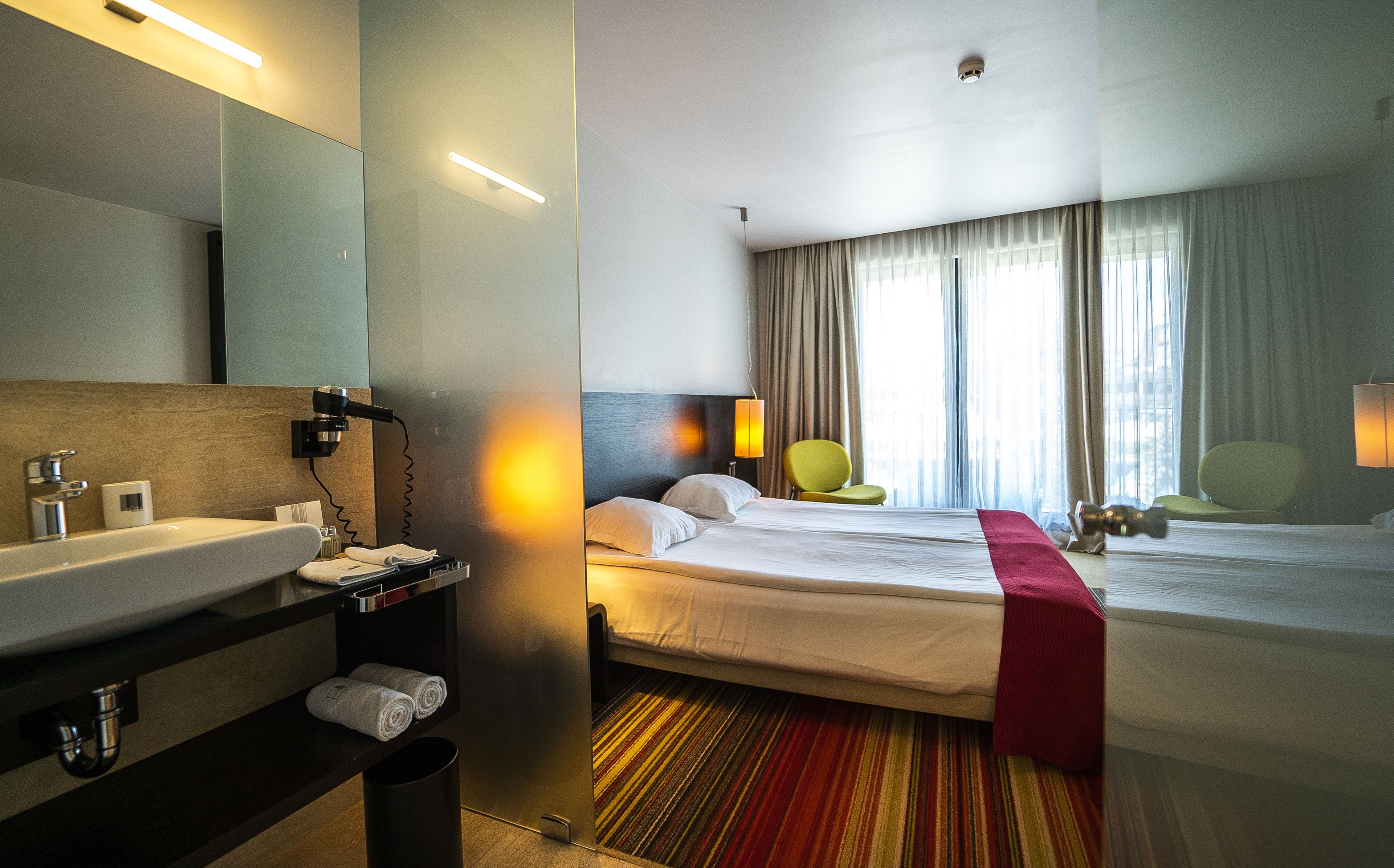A hotel room with a bed, a bathroom with a sink, and a mirror.